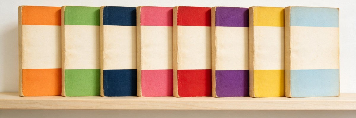 A row of eight vintage paperback books on a shelf, each with a plain three-band cover in a different colour: orange, green, navy, pink, red, purple, yellow and light blue