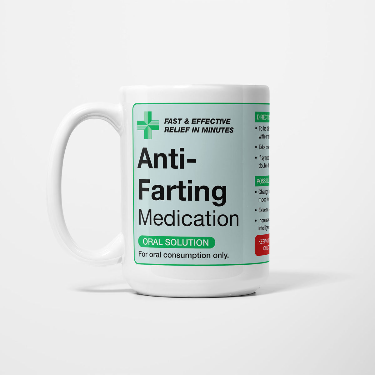 The 15oz Anti-Farting Medication mug, white ceramic with a pale green pharmacy label reading 'Anti-Farting Medication — oral solution, for oral consumption only', a green first-aid cross beside it