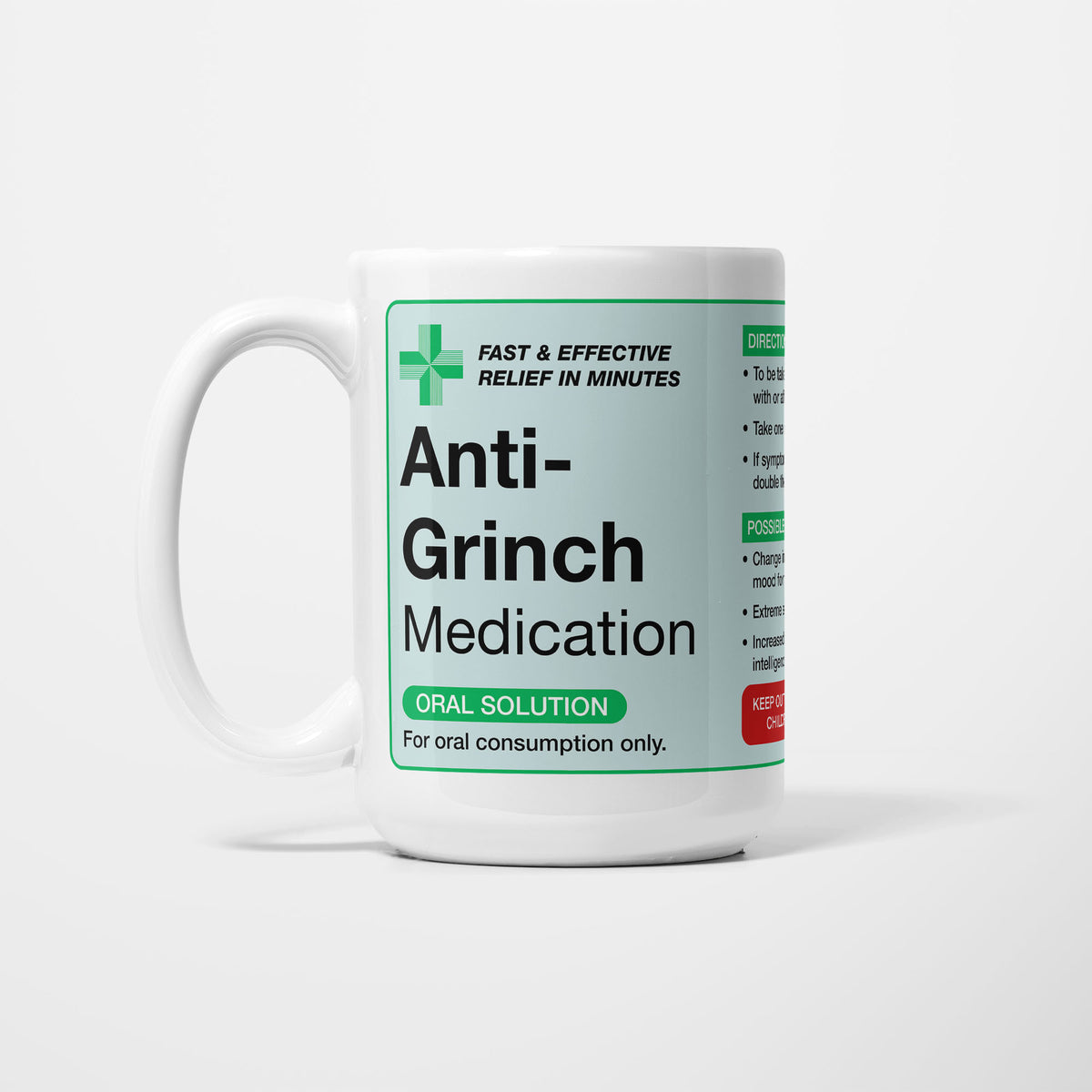 The 15oz Anti-Grinch Medication mug, white ceramic with a pale green pharmacy label reading 'Anti-Grinch Medication — oral solution, for oral consumption only', a green first-aid cross beside it