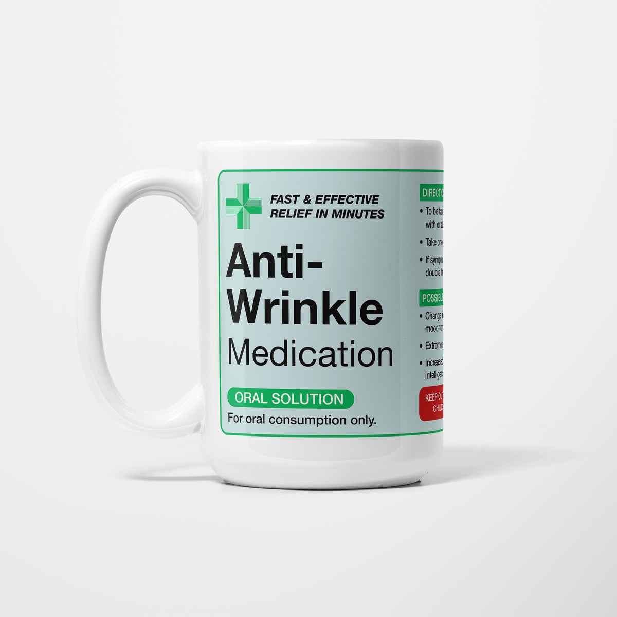 The 15oz Anti-Wrinkle Medication mug, white ceramic with a pale green pharmacy label reading 'Anti-Wrinkle Medication — oral solution, for oral consumption only', a green first-aid cross beside it