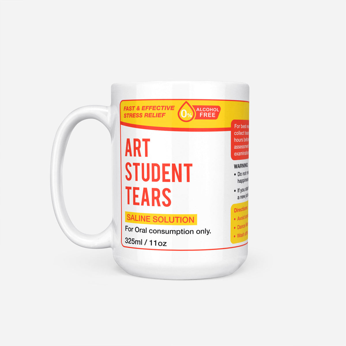 The 15oz Art Student Tears mug, white ceramic with a yellow pharmacy-style label reading 'Art Student Tears — Saline Solution, for oral consumption only'