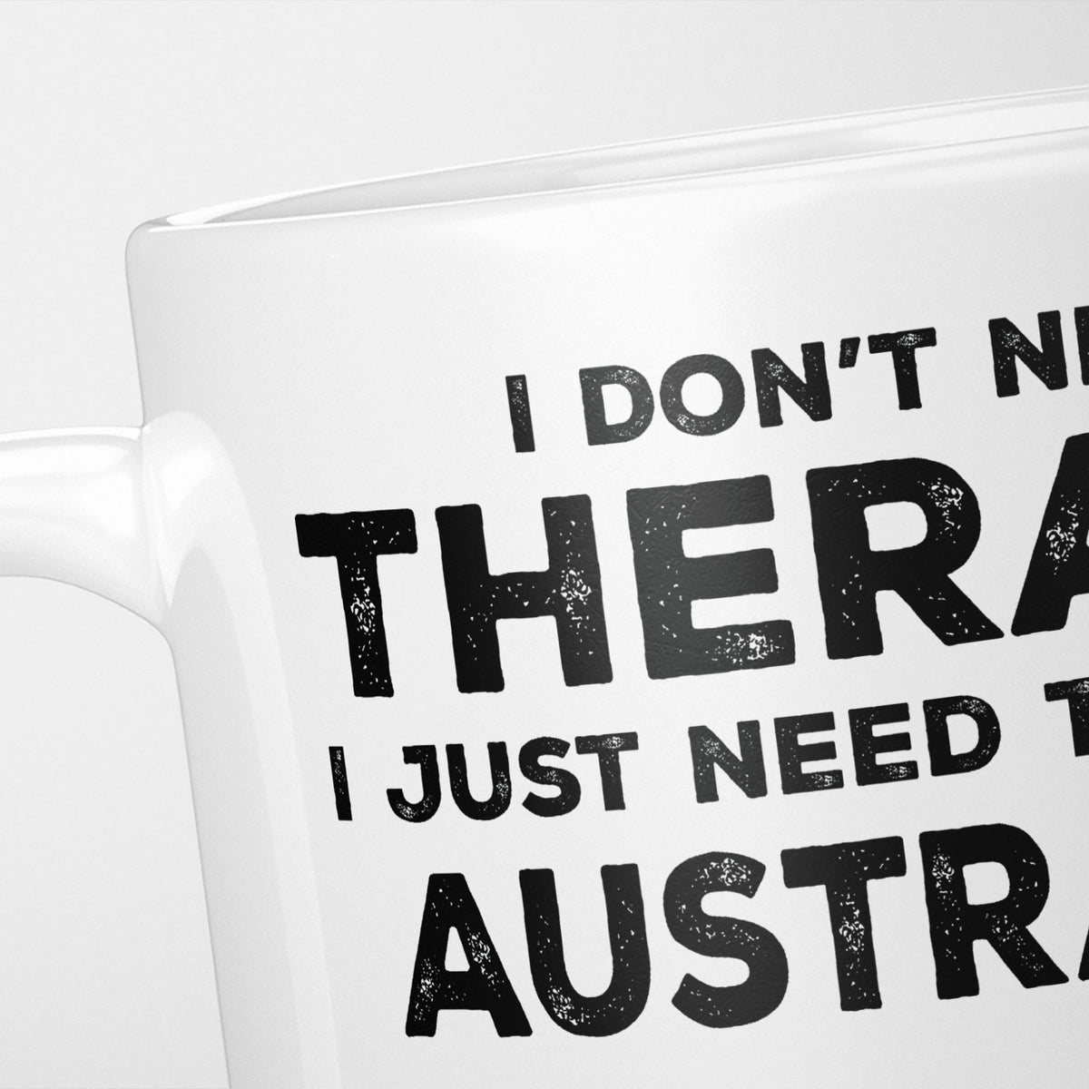Close crop of the I Need Australia mug, 'I don't need therapy, I just need to go to AUSTRALIA' in heavy distressed black type, running off the edges of the frame