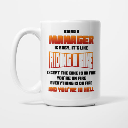 The 15oz Being A Manager Is Easy mug, white ceramic reading 'Being a MANAGER is easy. It's like RIDING A BIKE — except the bike is on fire, you're on fire, everything is on fire, and you're in hell' in orange, red and black