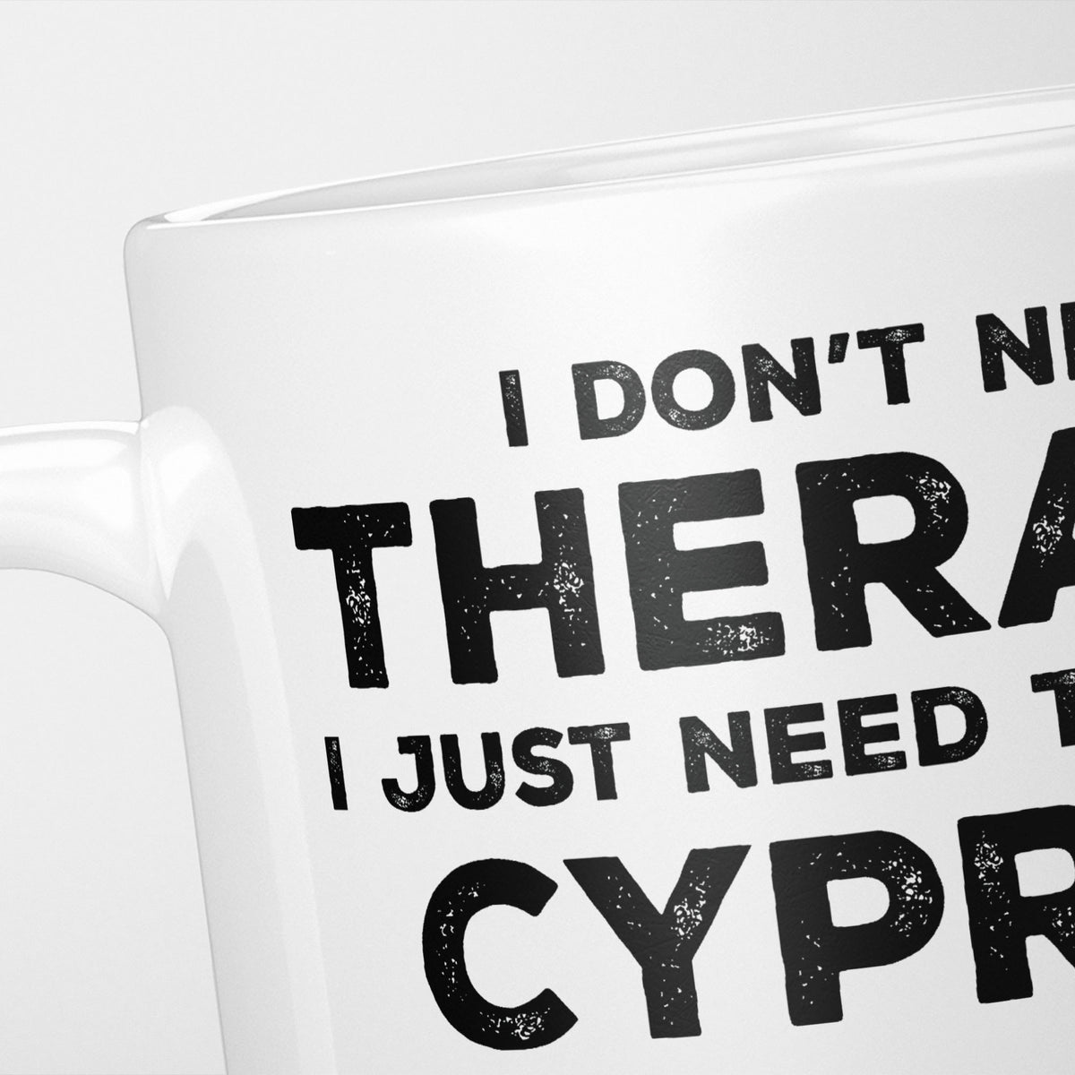 Close crop of the I Need Cyprus mug, 'I don't need therapy, I just need to go to CYPRUS' in heavy distressed black type, running off the edges of the frame