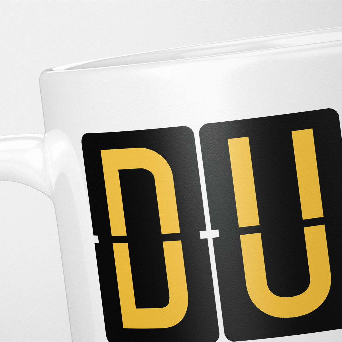 Close crop of the Dublin Airport Tag mug, gold split-flap tiles reading 'D' and 'U' on black — the first two letters of DUB