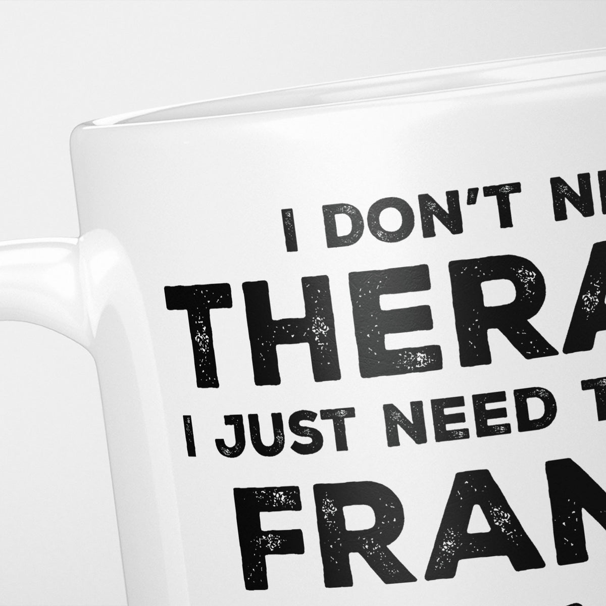 Close crop of the I Need France mug, 'I don't need therapy, I just need to go to FRANCE' in heavy distressed black type, running off the edges of the frame