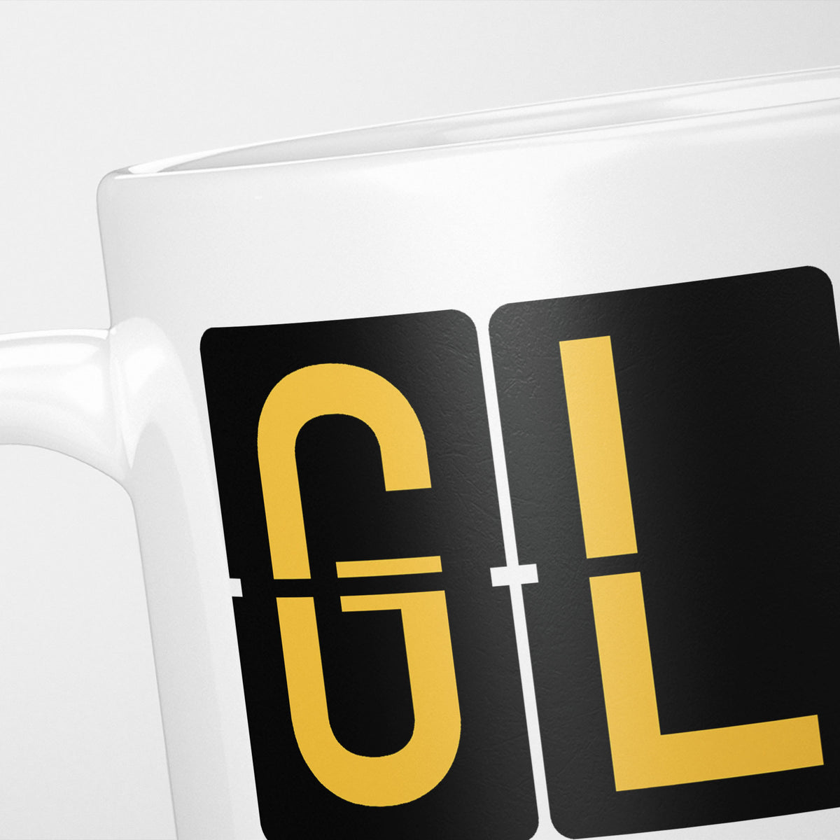 Close crop of the Glasgow Airport Tag mug, gold split-flap tiles reading 'G' and 'L' on black — the first two letters of GLA