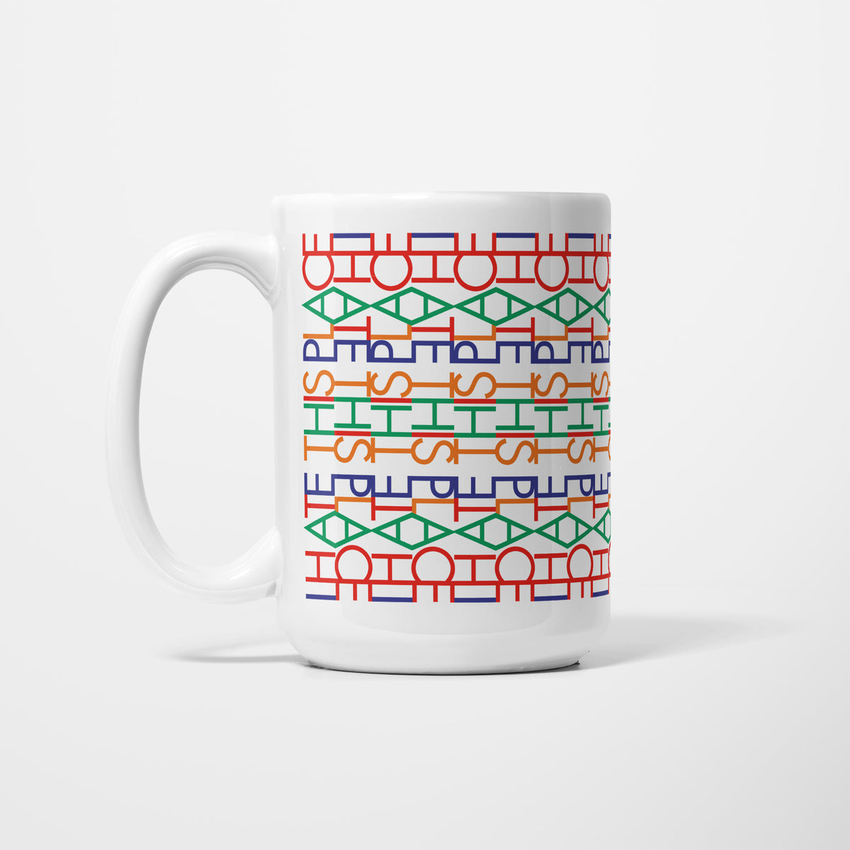Left side of the 15oz Funny Hidden Message "I Hate This Place" mug, white ceramic patterned with rows of interlocking letterforms in red, green, orange and blue that resolve into 'I hate this place' when read straight on