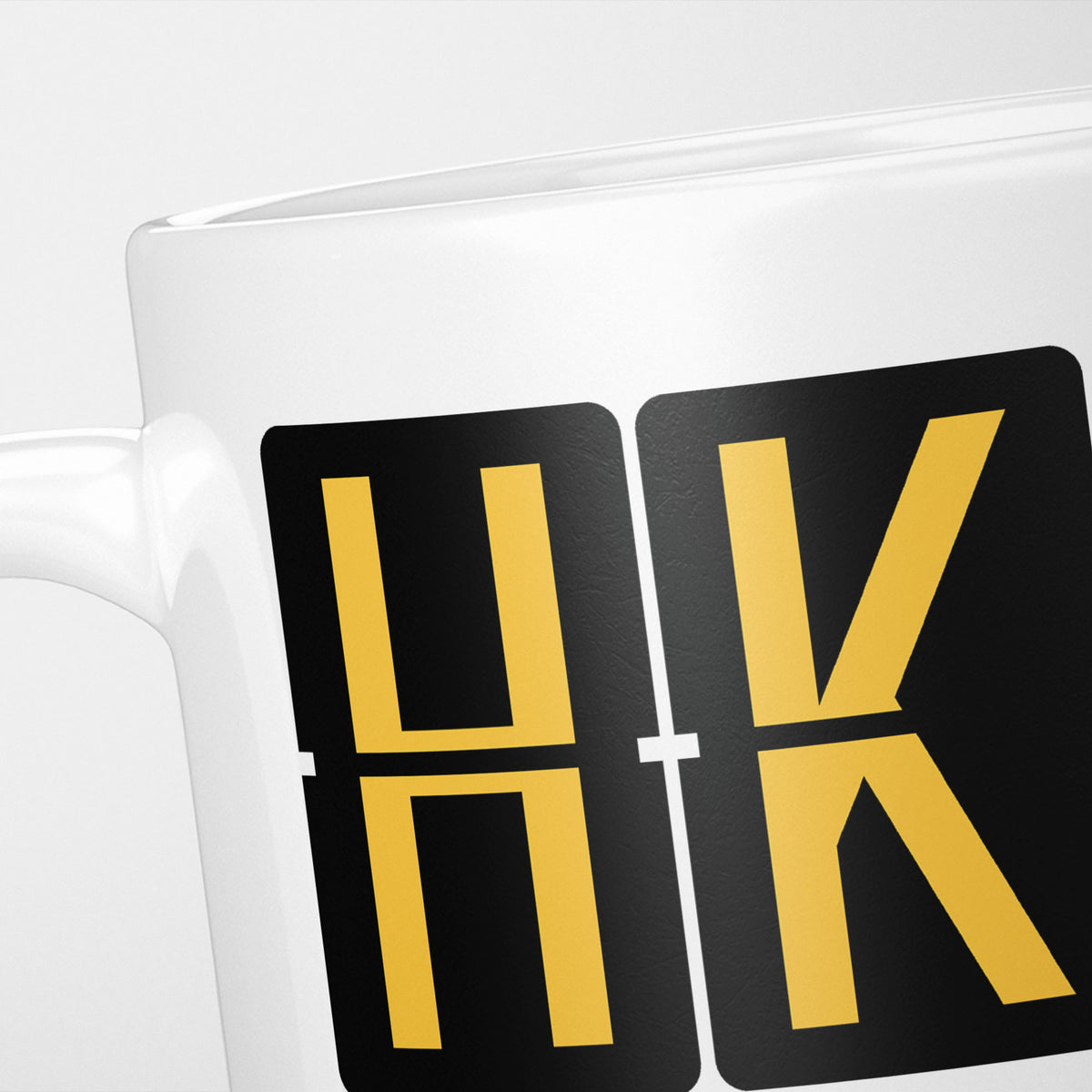 Close crop of the Hong Kong Airport Tag mug, gold split-flap tiles reading 'H' and 'K' on black — the first two letters of HKG