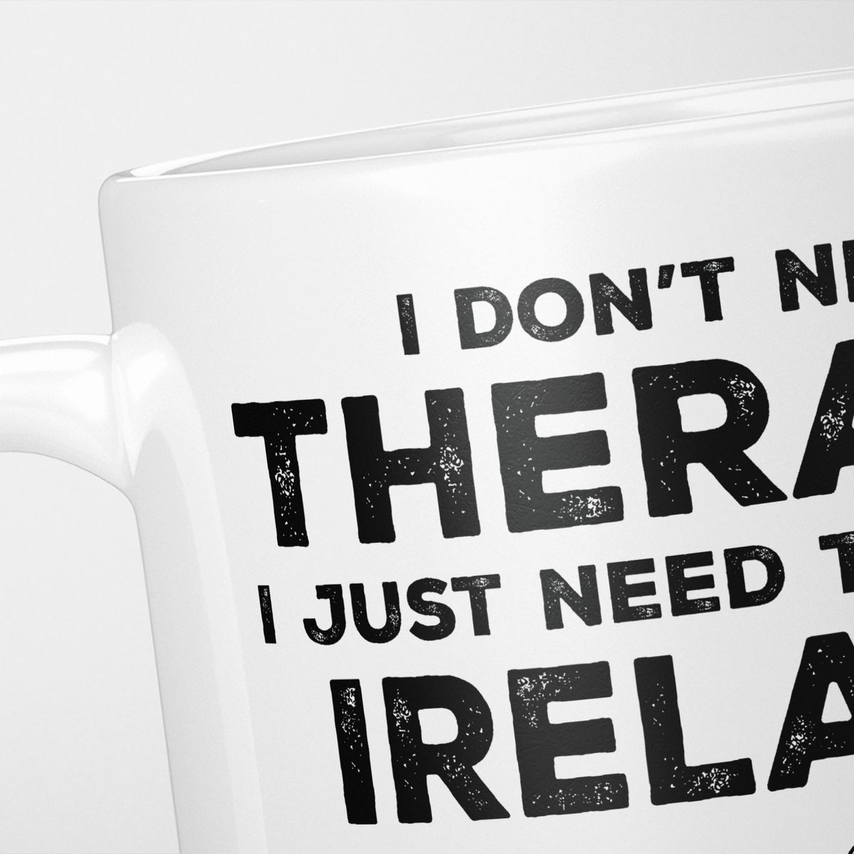Close crop of the I Need Ireland mug, 'I don't need therapy, I just need to go to IRELAND' in heavy distressed black type, running off the edges of the frame