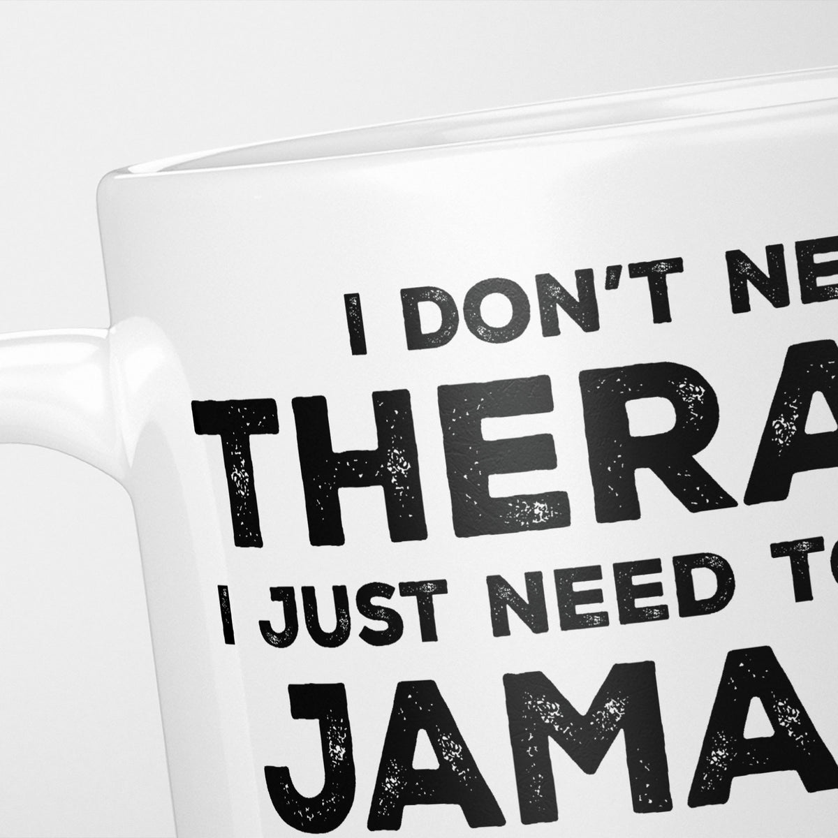 Close crop of the I Need Jamaica mug, 'I don't need therapy, I just need to go to JAMAICA' in heavy distressed black type, running off the edges of the frame