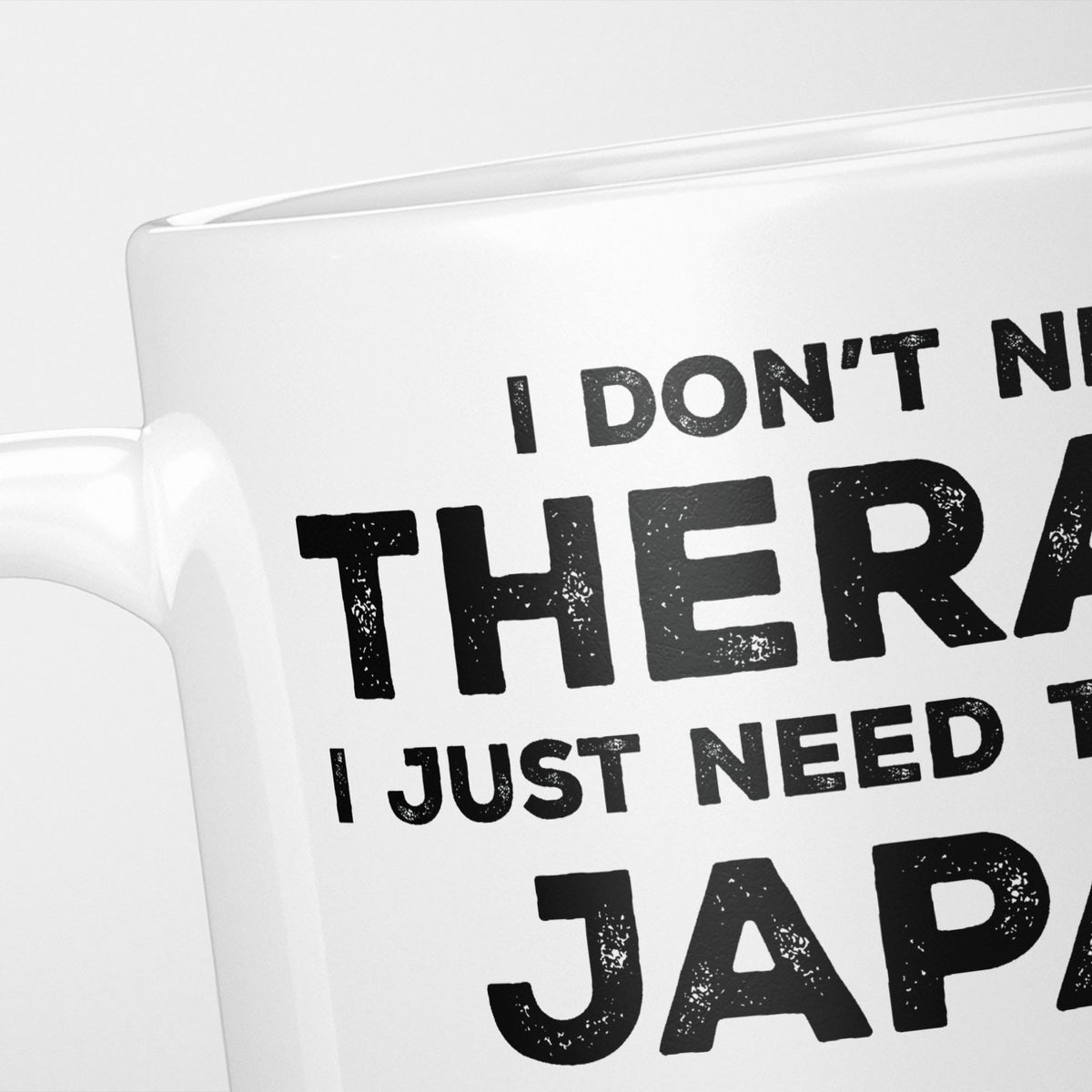 Close crop of the I Need Japan mug, 'I don't need therapy, I just need to go to JAPAN' in heavy distressed black type, running off the edges of the frame