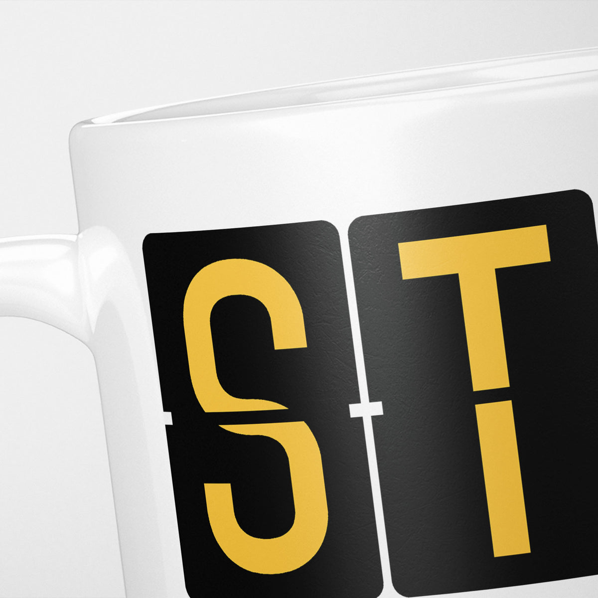 Close crop of the London Stansted Airport Tag mug, gold split-flap tiles reading 'S' and 'T' on black — the first two letters of STN
