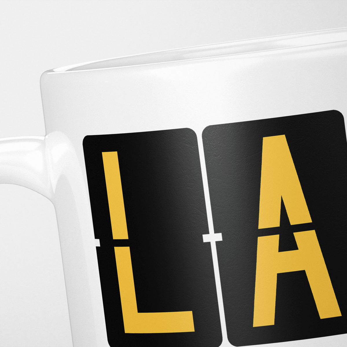 Close crop of the Los Angeles Airport Tag mug, gold split-flap tiles reading 'L' and 'A' on black — the first two letters of LAX