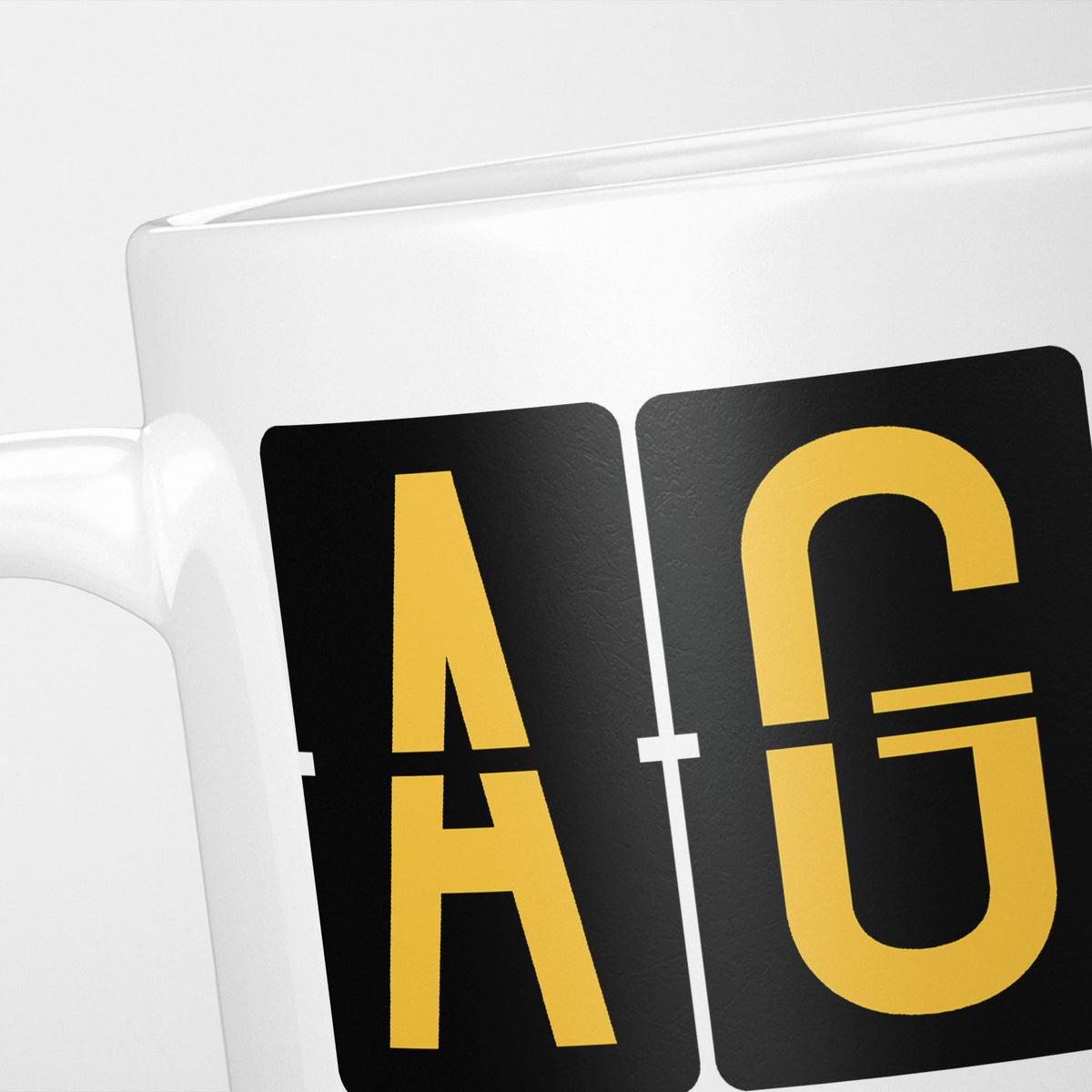 Close crop of the Malaga Airport Tag mug, gold split-flap tiles reading 'A' and 'G' on black — the first two letters of AGP