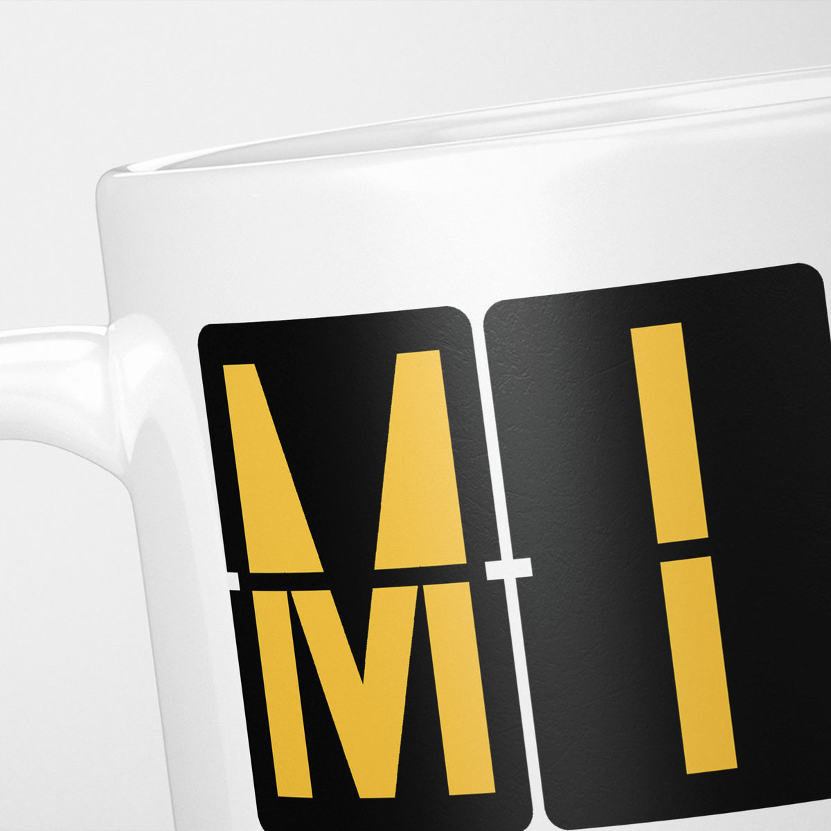 Close crop of the Miami Airport Tag mug, gold split-flap tiles reading 'M' and 'I' on black — the first two letters of MIA