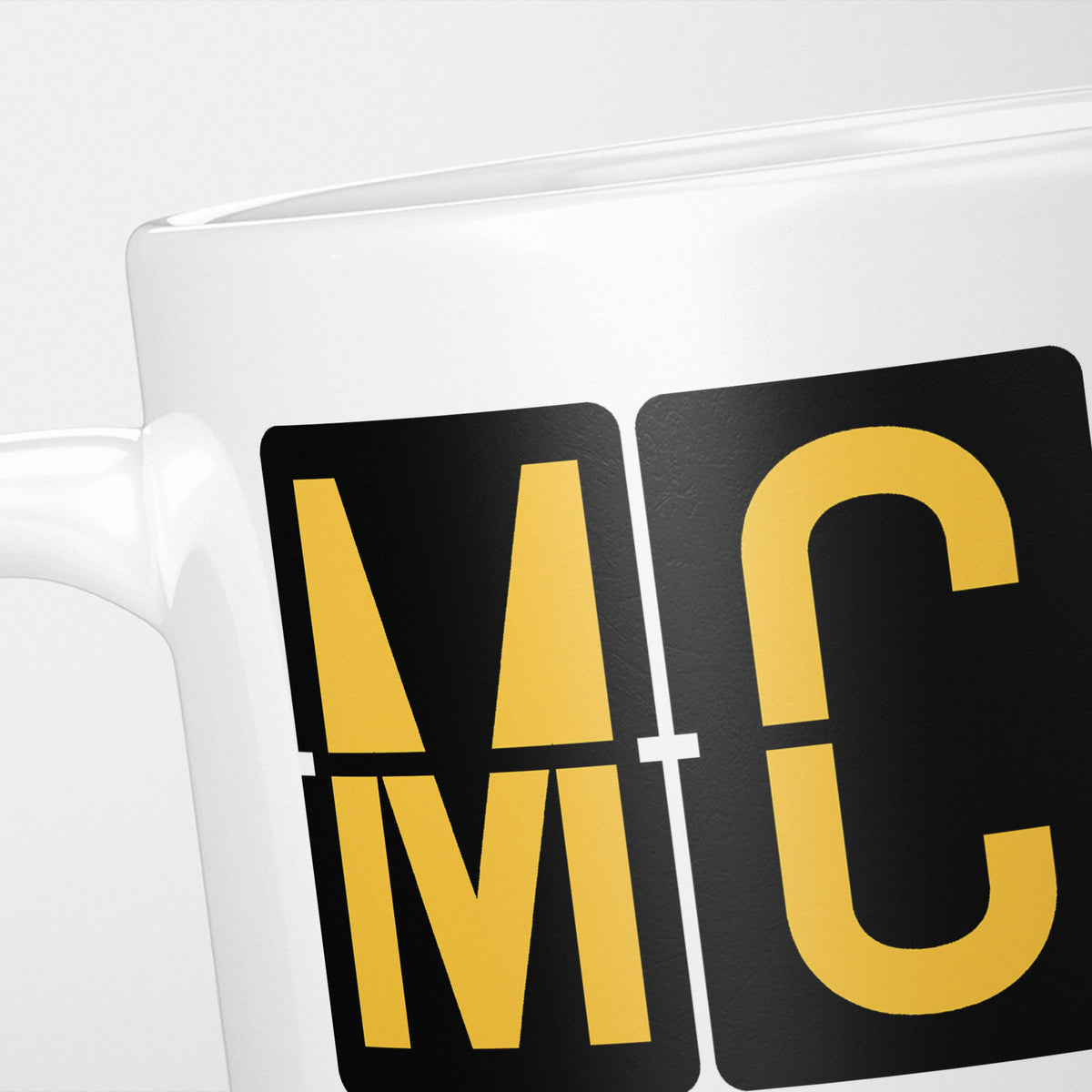 Close crop of the Orlando Airport Tag mug, gold split-flap tiles reading 'M' and 'C' on black — the first two letters of MCO