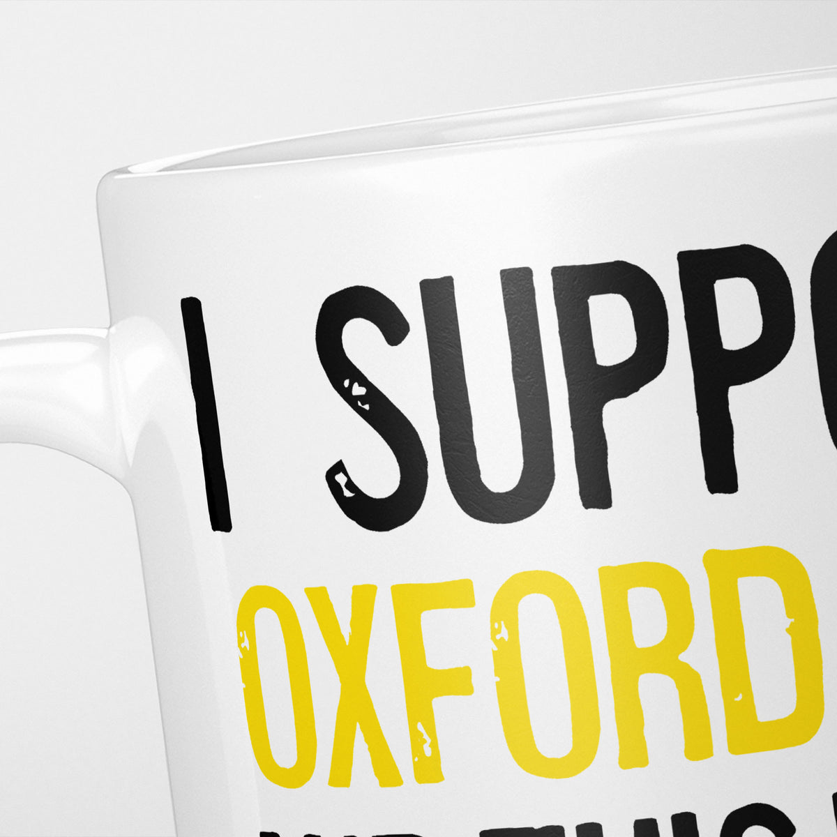 Close crop of the I Support Oxford Utd mug, 'I Support' in heavy black above the club name in yellow, running off the edge of the frame
