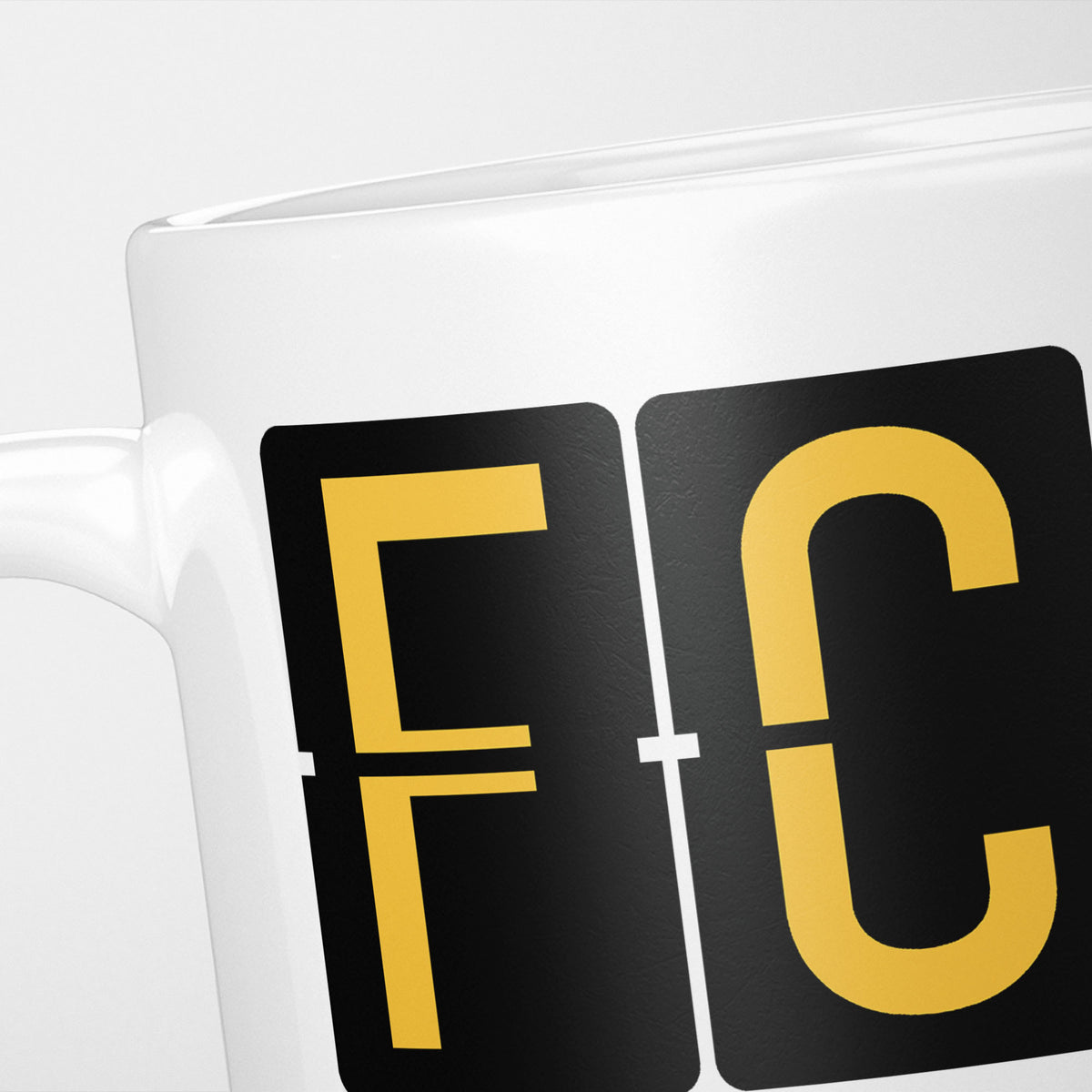 Close crop of the Rome Airport Tag mug, gold split-flap tiles reading 'F' and 'C' on black — the first two letters of FCO