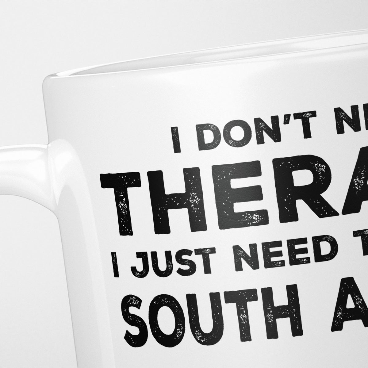 Close crop of the I Need South Africa mug, 'I don't need therapy, I just need to go to SOUTH AFRICA' in heavy distressed black type, running off the edges of the frame