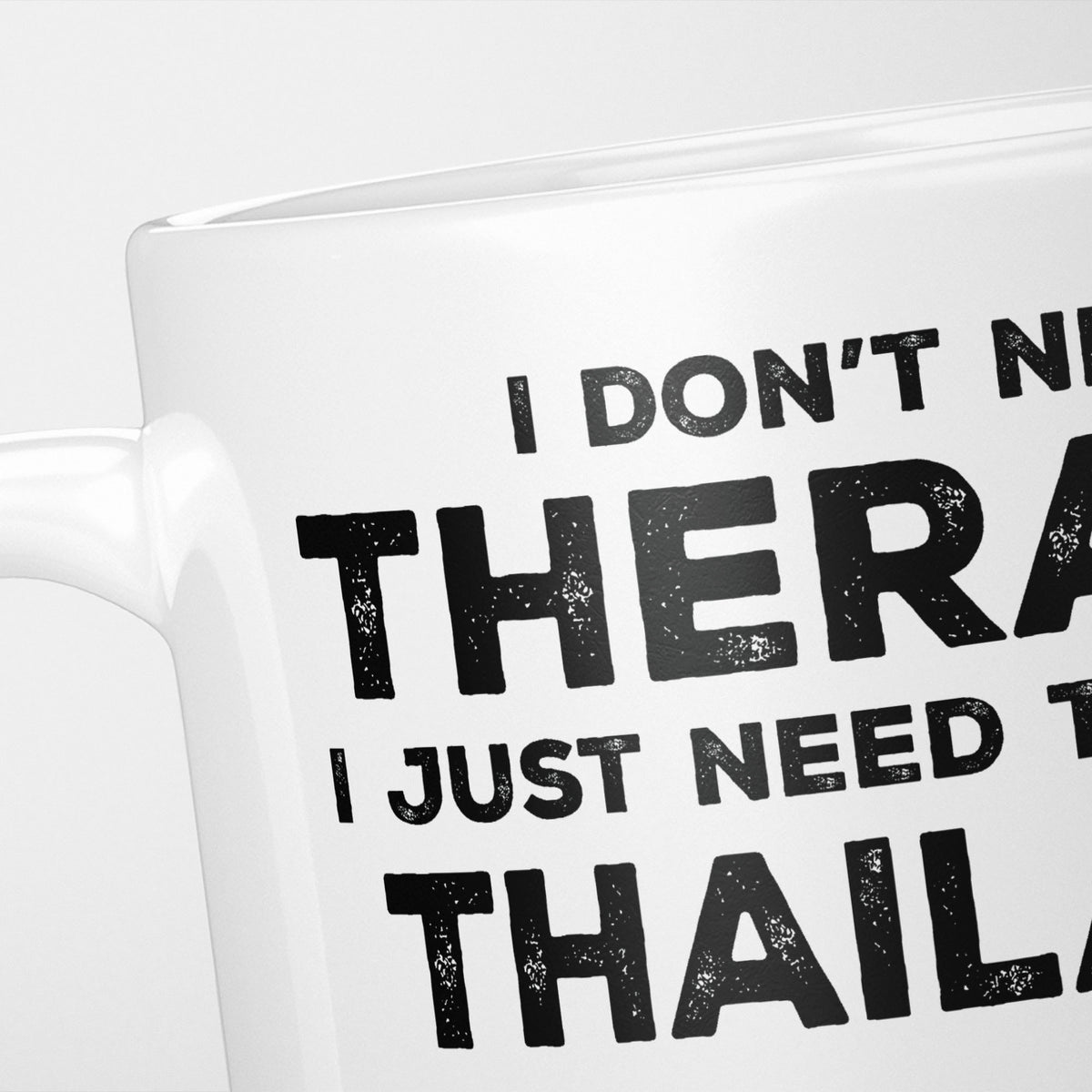 Close crop of the I Need Thailand mug, 'I don't need therapy, I just need to go to THAILAND' in heavy distressed black type, running off the edges of the frame