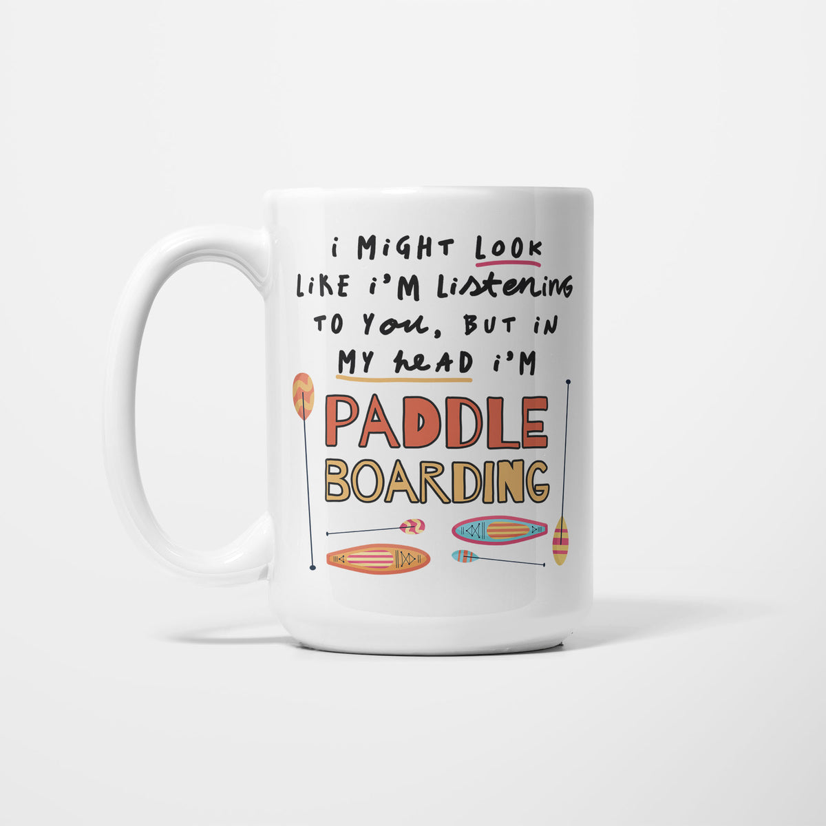 White 15oz ceramic mug, hand-lettered "I might look like I'm listening to you, but in my head I'm Paddle Boarding" in orange and yellow, illustrated with three paddleboards and paddles