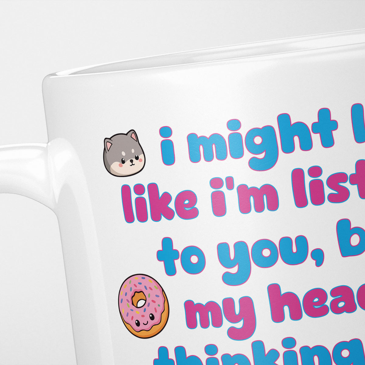 Close crop of the I'm Thinking About Squishies mug, the opening of the rounded pink and blue lettering, with a kawaii grey cat and a sprinkled doughnut alongside