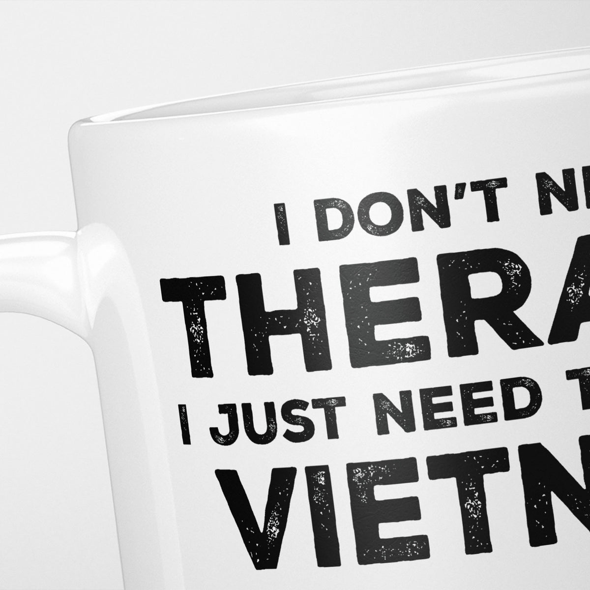 Close crop of the I Need Vietnam mug, 'I don't need therapy, I just need to go to VIETNAM' in heavy distressed black type, running off the edges of the frame