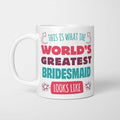 White ceramic mug in retro pink, plum and teal typography reading 'This is what the World's Greatest Bridesmaid looks like', with two curved arrows pointing up at the person holding it and starbursts either side