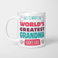 White ceramic mug in retro pink, plum and teal typography reading 'This is what the World's Greatest Grandma looks like', with two curved arrows pointing up at the person holding it and starbursts either side