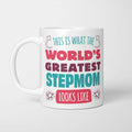 White ceramic mug in retro pink, plum and teal typography reading 'This is what the World's Greatest Stepmom looks like', with two curved arrows pointing up at the person holding it and starbursts either side